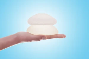 The image shows a hand holding two breast implants, illustrating the options available in the breast augmentation process. Find out more about the types of implants and procedures in our article.