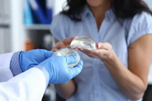 The image shows a doctor showing a patient the details of a breast implant, including its appearance, texture, and the material it is made of. Learn more about the breast augmentation process and the options available in our specialized article.